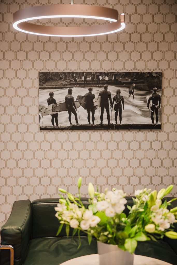 Blick auf ein Bild der Eisbachwelle in schwarz-weiß vor gemusterter Tapete