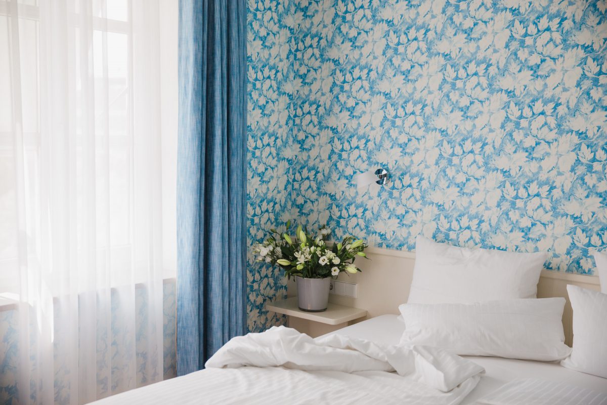 View of a double bed next to colorful flowers and a white and turquoise patterned wall 