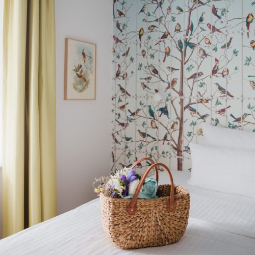 Basket on a hotel bed with wallpaper in bird pattern in the background